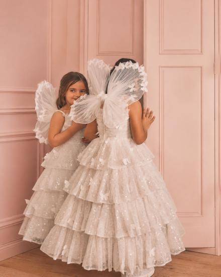 Mädchen in festlichen Kinderkleidern mit Feenflügeln im rosa Zimmer